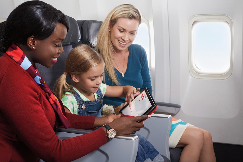 Un agent de bord d’Air Canada Rouge explique à une maman et à sa fille le fonctionnement de lectuer, le système divertissement en vol.